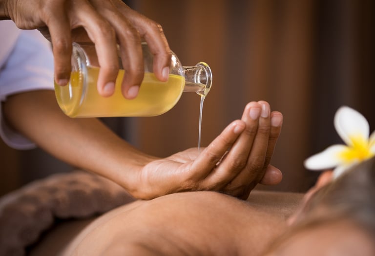Therapist pouring essential massage oil onto hands for a relaxing spa body treatment.