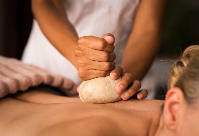 Professional massage therapist performing a herbal compress massage on a woman's back in a spa.