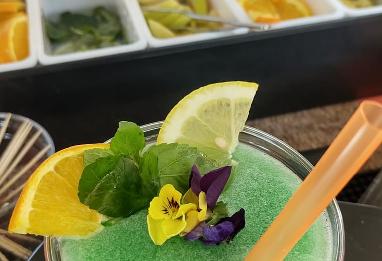 Coctel frappé verde adornado con menta fresca, rodajas de cítricos y flores comestibles
