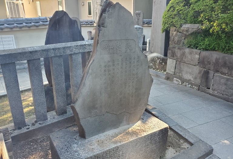A traditional Japanese stone monument with kanji inscriptions in a Buddhist temple garden.