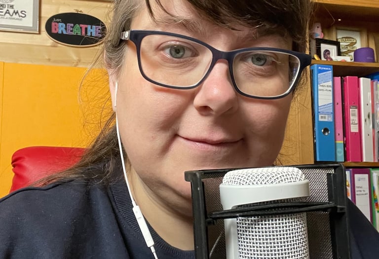 Laura Dumbleton at her recording setup with a microphone and BREATHE sign on the wall behind her