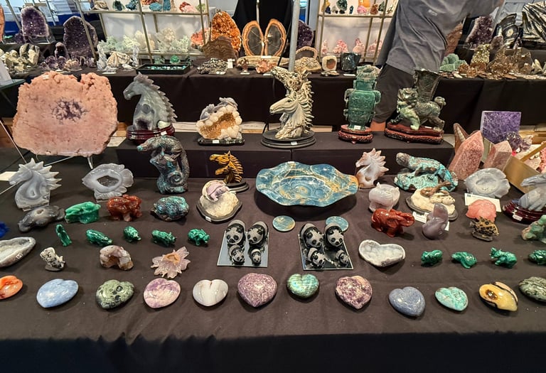 A collection of colorful polished gemstones and crystal animal carvings displayed on a table at a gem show.