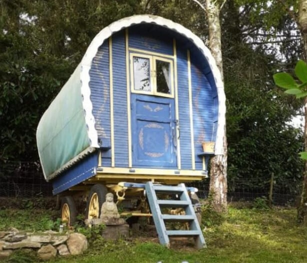 Colorful bow-top gypsy wagon with blue and yellow paint, garden roulotte with ladder entrance, Buddh