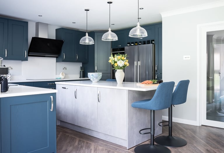 Modern kitchen featuring blue shaker cabinets, a light grey island with seating, and pendant lighting.