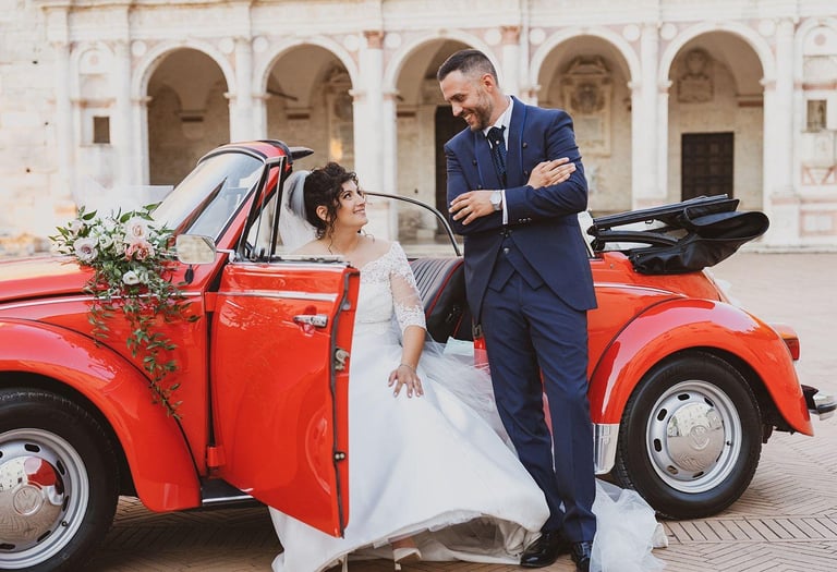 Sposi sorridenti a bordo del maggiolone rosso addobbato per il loro matrimonio