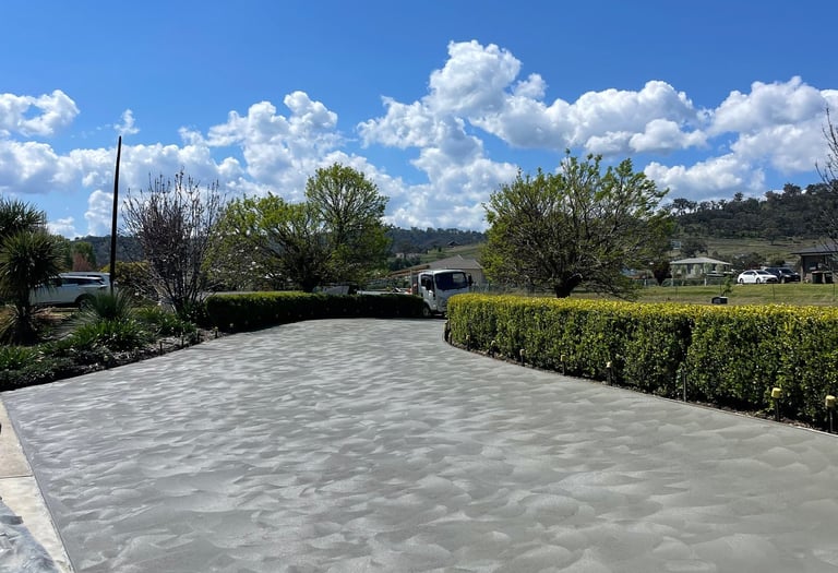 Freshly poured decorative concrete driveway with hand-troweled swirl finish in a residential landscape.