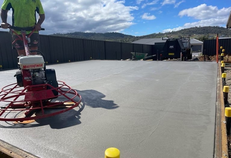 Professional concreter using a power trowel machine to finish a fresh concrete slab for a backyard patio.