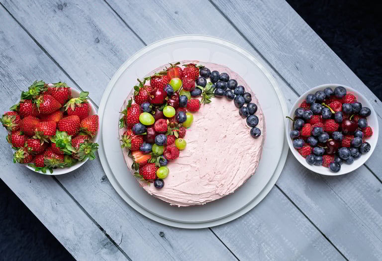 a cake with fruit on a table with bowls of fruit