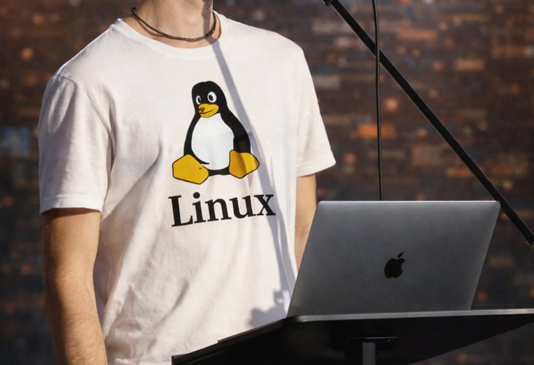 A man in a Linux penguin t-shirt giving a presentation with a MacBook and microphone.