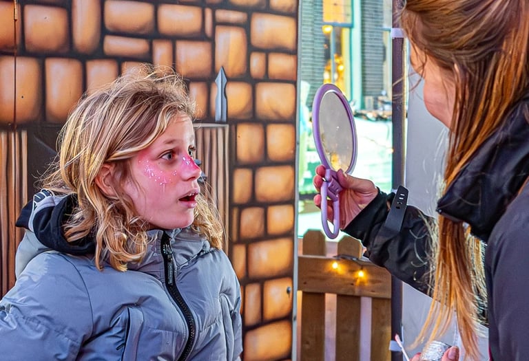 Een meisje kijkt vol bewondering naar haar roze schminkcreatie in een handspiegel.