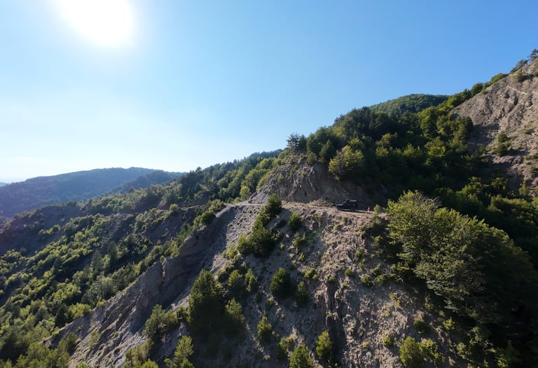 Off-road vehicle parked on a steep cliffside mountain trail overlooking a lush green forest valley.