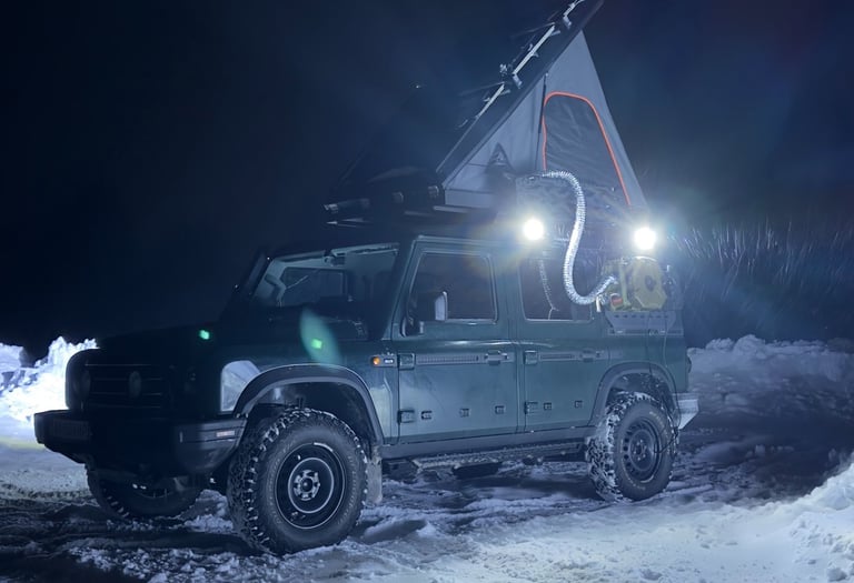 Off-road 4x4 vehicle with a rooftop tent and diesel heater setup for winter camping in the snow at night.