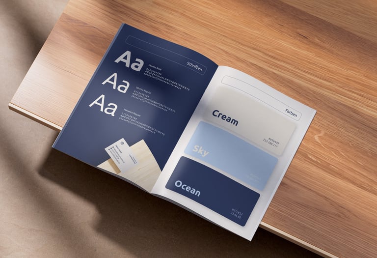 Aufgeklappte Broschüre in inklusivstudio-Farben auf Holzplatte