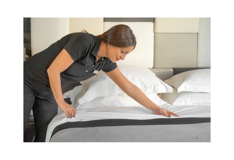 Professional housekeeper making a bed in a clean and organized guest bedroom.
