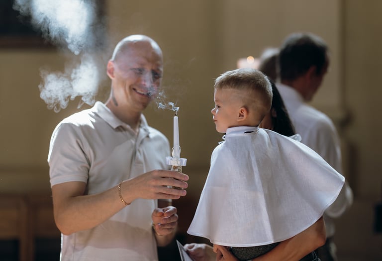 Krikštynų fotografija - krikšto tėtis laiko rankose žvakę, kurią ką tik užpūtė berniukas