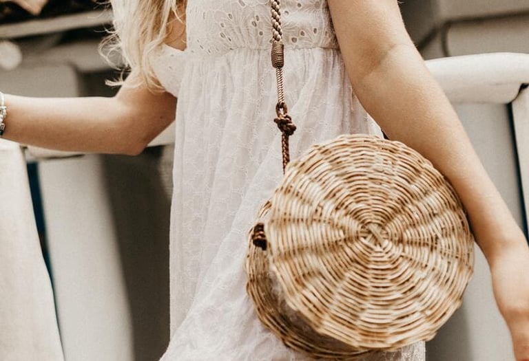 Una mujer usando un bolso bandolera redondo de paja tejida como parte de un atuendo veraniego.