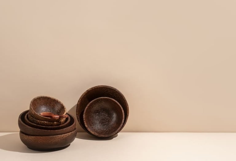 Cuencos artesanales de madera oscura y una pequeña cuchara de madera apilados sobre un fondo beige 