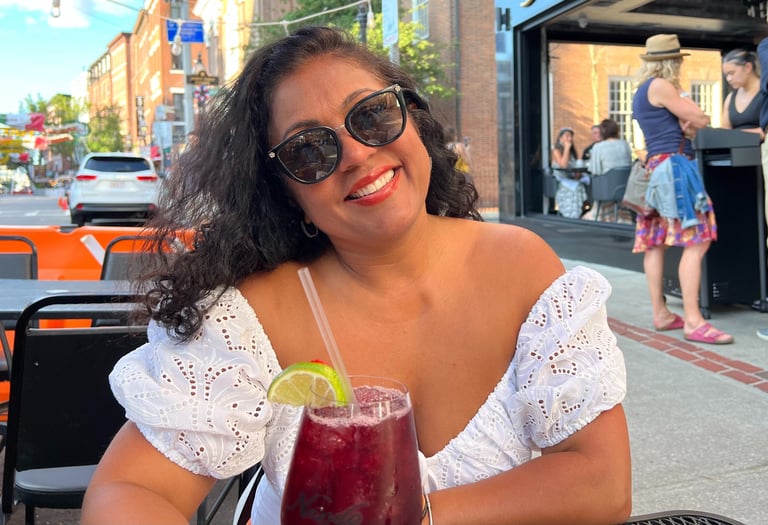 Smiling woman in a white eyelet top enjoying a red sangria cocktail at an outdoor city patio