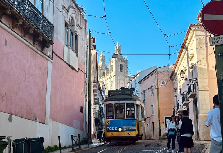 Uma estrada estreira entre as casas portuguesas, com um bondinho ao meio e a catedral ao fundo.