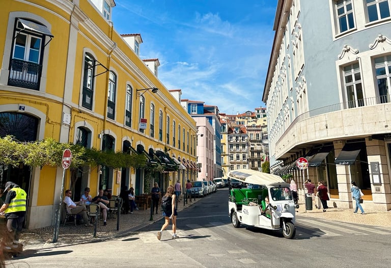 Prédios, um estrada, pessoas em bares e um tuk tuk