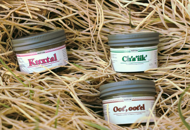 Tres frascos de pomadas herbales naturales mayas, colocados sobre paja seca 