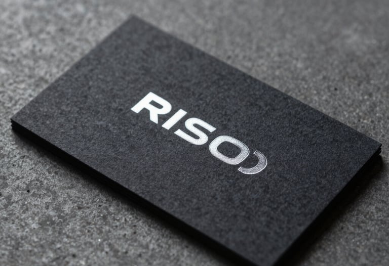 Macro photography of a sleek, dark-textured business card with silver foil lettering, resting on a charcoal gray concrete surface.