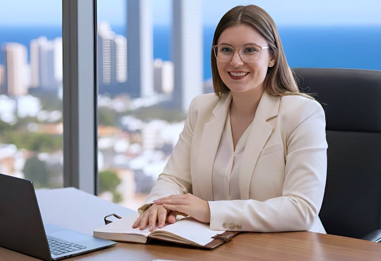 mujer joven sonriente sentada en oficina con vistas a Benidorm, con un ordenador y libreta en la mes