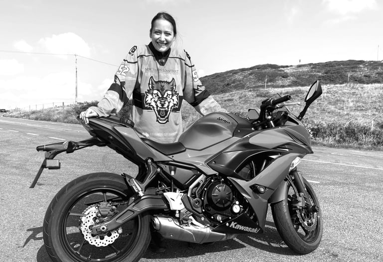 A young rider called Becky stood behind her motorcycle in a countryside landscape