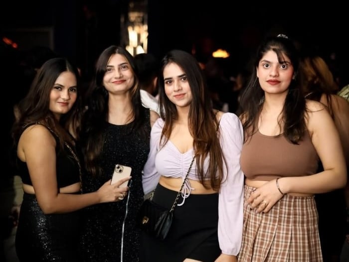 a group of women standing around a man in a brown top