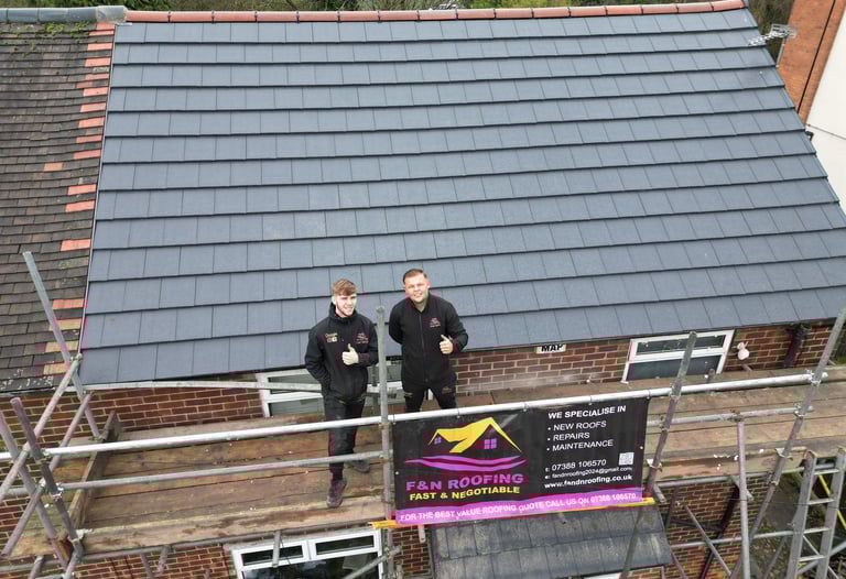 Professional roofing contractors standing on scaffolding after completing a modern grey tile roof installation.