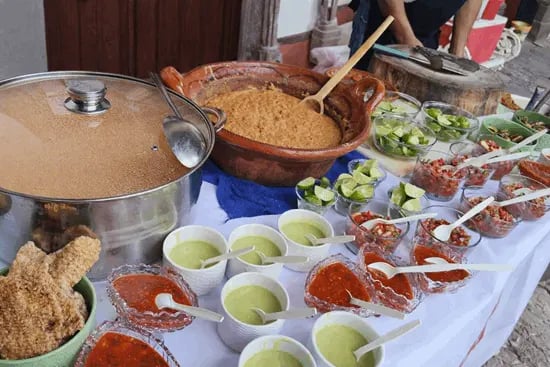 Mesa de servicio para evento con olla de frijoles, cazuela y salsas roja, limones y guarniciones