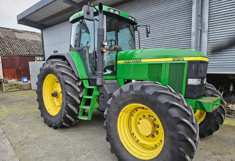 A green and yellow John Deere 7810 tractor parked on a farm beside a metal barn.