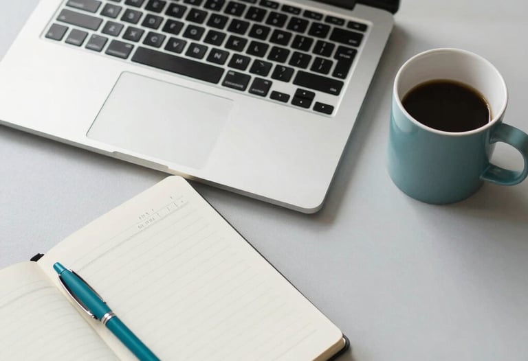 A top-down, clean desk composition in a North American office. A sleek laptop, a branded notebook with a teal pen, and a ceramic mug sit on a light grey surface. The lighting is bright and natural, reflecting a productive and professional digital marketing environment.