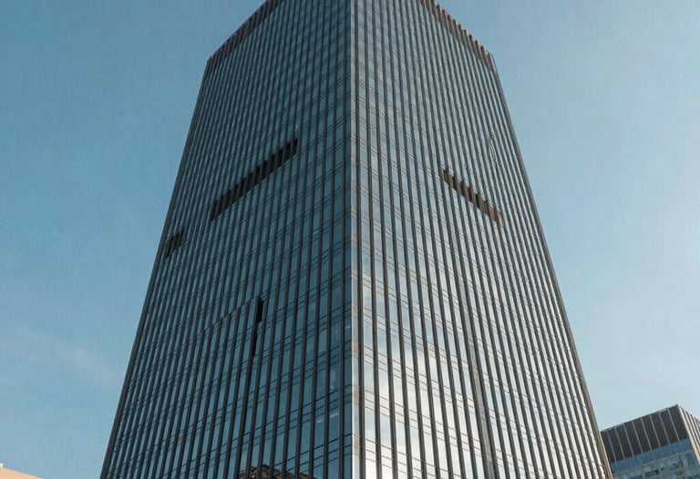 A wide shot of a modern glass skyscraper reflecting a clear blue sky, low angle, representing corporate growth and innovation. International city.
