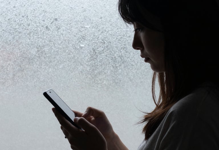 A subtle shot of a woman's silhouette against a frosted glass window, holding a phone down by her side, symbolizing a moment of choosing presence over the screen.