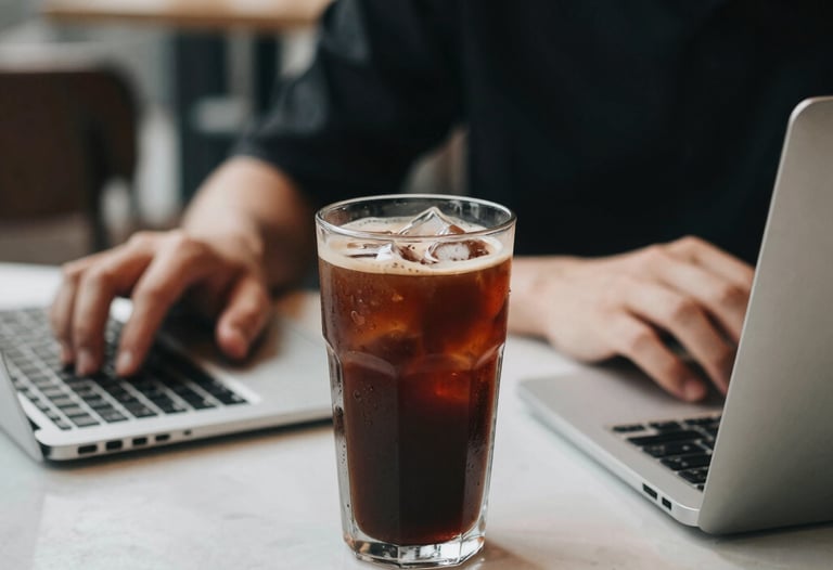 A glass of iced coffee next to a focused person's workspace in a chic Ho Chi Minh City cafe. The lighting is crisp and the vibe is productive and trendy.