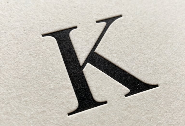 Close-up of a high-fashion serif font printed on premium thick off-white paper. Letterpress texture visible. Minimalist and elegant.