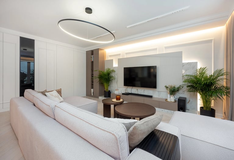 Nowoczesny salon z jasną sofą, stolikiem kawowym, telewizorem na ścianie i dużymi oknami