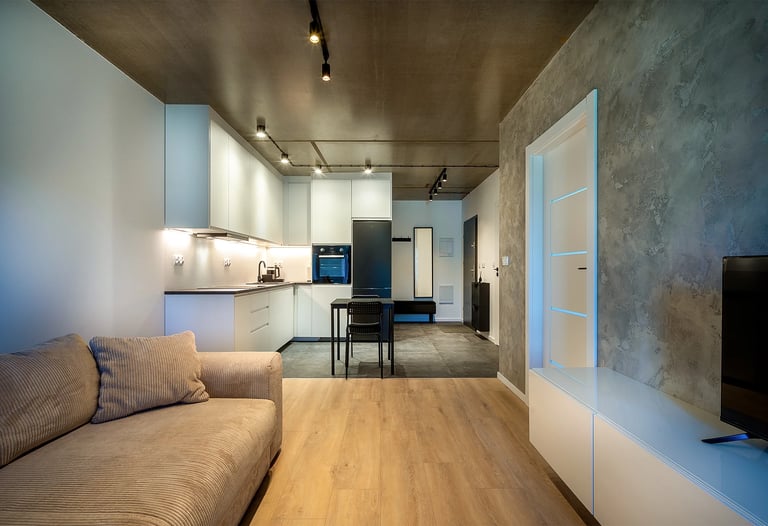 Nowoczesny salon z aneksem kuchennym, jasne meble, betonowy sufit i ściana TV.