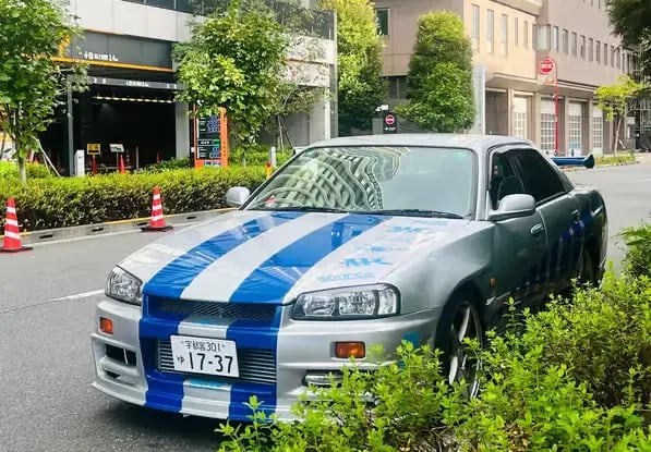 Silver Nissan Skyline R34 GT-R replica driving on Tokyo streets.
