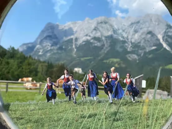 Children in traditional outfits running through a green Alpine meadow.