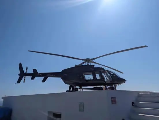 Private charter helicopter parked on rooftop helipad under clear Aegean blue sky