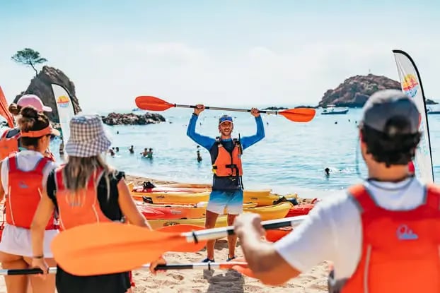 Certified sea kayak instructor holding paddle on Tossa de Mar beach with group and kayaks