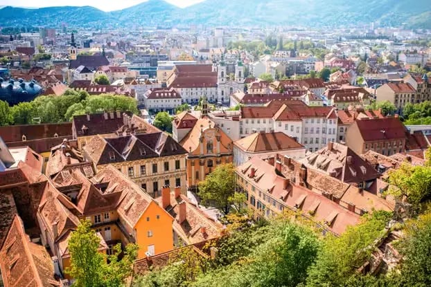 Wide panoramic view of Graz city rooftops and surrounding mountains from Schlossberg.