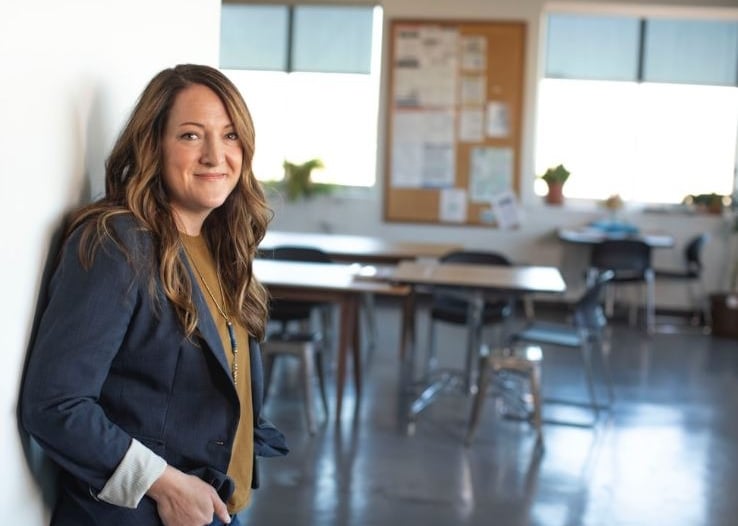 a female teacher standing in a room with a desk and chairs