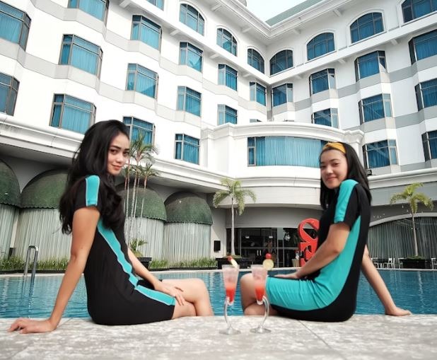 two hospitality workers in blue dresses sitting by a hotel swimming pool 