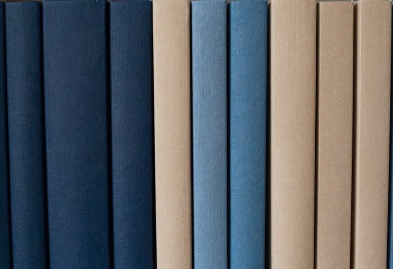 A row of journals lined up on a shelf, showing a gradient of blues and beiges. The shot is minimalist and calm, emphasizing order and curation. Southeast Asian context.