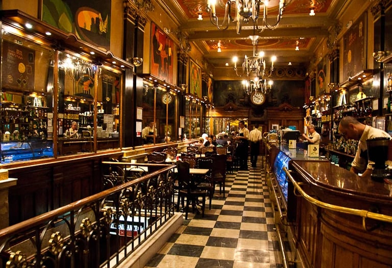 Historic European cafe interior featuring checkered floors, ornate gold accents, and a classic wooden bar.