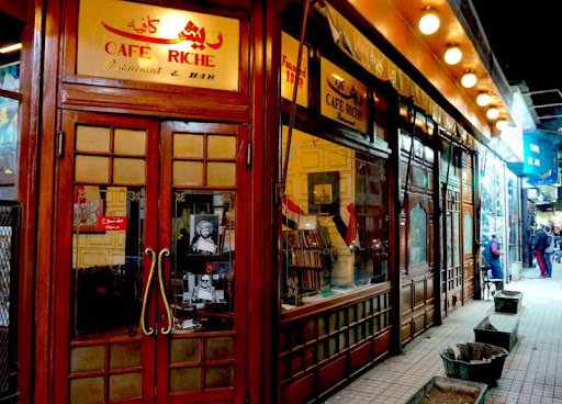 The historic wooden facade and entrance of Cafe Riche restaurant and bar in downtown Cairo at night.