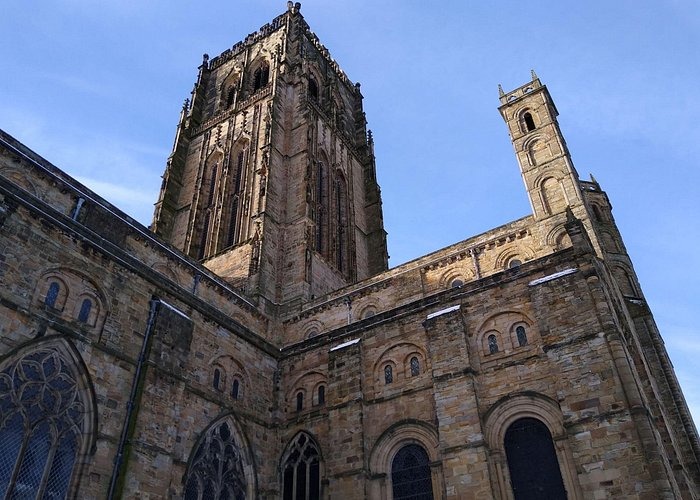 Low-angle view of the historic Durham Cathedral stone towers and gothic architecture against a blue sky.